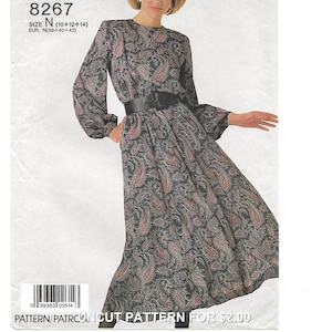 May include: A sewing pattern envelope labeled 8267, size N (10+12+14), featuring a long-sleeved dress with a dark grey and red paisley print, a high neckline, and a wide black belt. The pattern is for a mid-length dress with gathered sleeves.