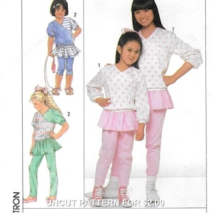 Puede incluir: Patrón de costura para dos conjuntos de niños. El patrón incluye una blusa de manga larga con un dobladillo con volantes y pantalones a juego. La blusa tiene un estampado de lunares. Los conjuntos se muestran en rosa y blanco. El patrón no está cortado y cuesta 2,00 €.