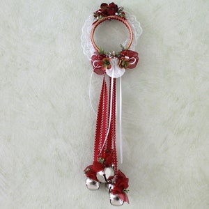 May include: A decorative Christmas ornament featuring a wooden embroidery hoop adorned with red flowers, white lace, and red and white ribbons. Silver bells hang from the bottom, adding a festive touch. The ornament is designed for hanging.