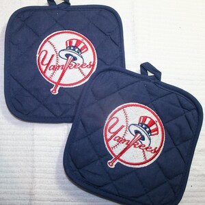 May include: Two navy blue quilted pot holders with the New York Yankees logo embroidered in red, white, and blue. The logo features a baseball with a bat and the word "Yankees". Each pot holder has a small loop for hanging.