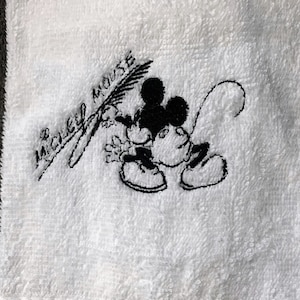 May include: White towel with black embroidered Mickey Mouse design and the text "Mickey Mouse".