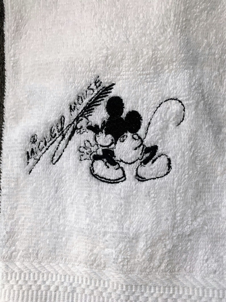 May include: White towel with black embroidered Mickey Mouse design and the text "Mickey Mouse".