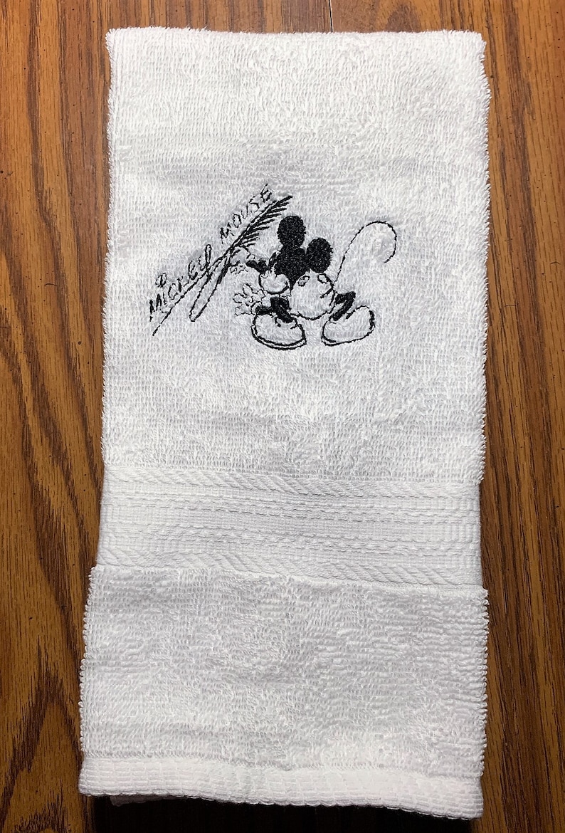 May include: White hand towel with black embroidered Mickey Mouse image and the text "Mickey Mouse".