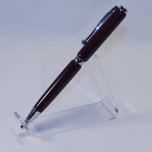May include: A burgundy and silver pen displayed on a clear acrylic stand. The pen has a shiny, metallic finish on the silver components and a smooth, polished barrel. The pen is angled slightly, showcasing its design.