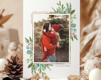 May include: A rectangular Christmas greeting card featuring a central photograph of an adult holding a child, framed by a gold border. The card includes watercolor illustrations of green pine branches and red holly berries, with the text "HAVE A VERY MERRY CHRISTMAS" and "THE SMITH FAMILY."