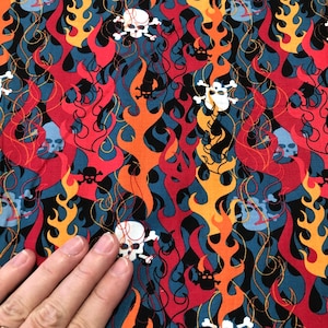 May include: A blue fabric with a repeating pattern of red, orange, and yellow flames with white skull and crossbones. The fabric has a black background.