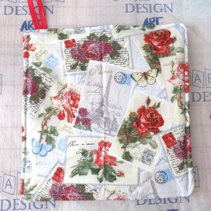 May include: Square, quilted pot holder with a red ribbon loop. The fabric features a collage of vintage postcards with red roses, butterflies, and the Eiffel Tower. The background is off-white with a subtle pattern.
