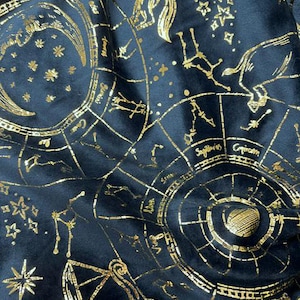 May include: A dark navy blue fabric featuring a metallic gold foil print of zodiac signs, constellations, and astrological charts. The pattern includes circular diagrams with labels for Sagittarius, Capricorn, and other signs, alongside stars.