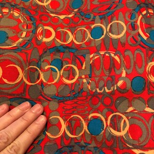May include: Red fabric with a repeating pattern of overlapping circles in shades of brown, beige, and teal.