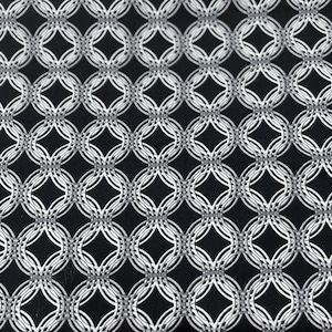 May include: Close-up of a black fabric with a repeating pattern of interconnected, white, oval shapes. The design creates a lattice-like effect, with diamond shapes formed at the intersections. The fabric has a textured appearance.