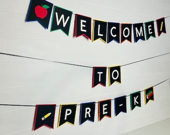 Może przedstawiać: Baner z napisem "WELCOME TO PRE-K" w białych literach na czarnych proporczykach. Każdy proporczyk ma kolorową obwódkę i jest nawleczony na czarny sznurek. Pierwszy proporczyk ma czerwone jabłko, a ostatni książki.