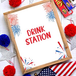 Könnte beinhalten: Ein gerahmtes Schild mit weißem Hintergrund und rotem Text, auf dem "DRINK STATION" steht. Das Schild ist mit roten, weißen und blauen Feuerwerkskörpern verziert. Das Schild ist umgeben von roten, weißen und blauen Pompons, silbernen Sternen und einer amerikanischen Flagge.