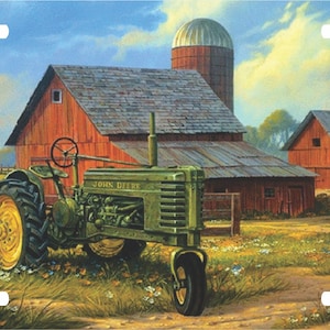 May include: A green John Deere tractor parked in front of a red barn with a silo. The tractor is in a field with a dirt road leading to the barn. There are trees and a fence in the background.