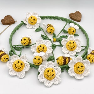 May include: A crocheted mobile with white daisy flowers and yellow and brown bees. The mobile is hanging from a wooden hoop.