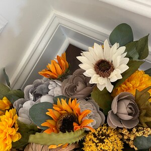 Peut inclure: Une composition florale sur le th&egrave;me de l'automne avec des tournesols, des marguerites blanches, des roses grises et des fleurs jaunes. L'arrangement est plac&eacute; dans une citrouille tiss&eacute;e.