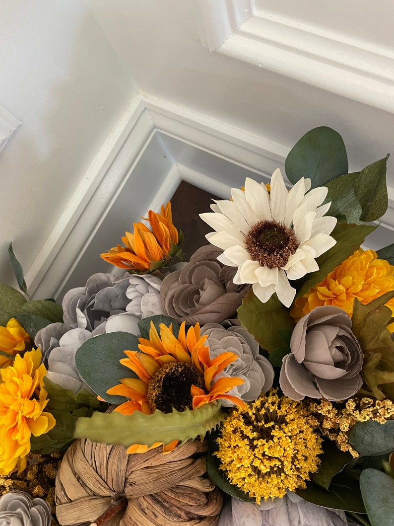Peut inclure: Une composition florale sur le th&egrave;me de l'automne avec des tournesols, des marguerites blanches, des roses grises et des fleurs jaunes. L'arrangement est plac&eacute; dans une citrouille tiss&eacute;e.