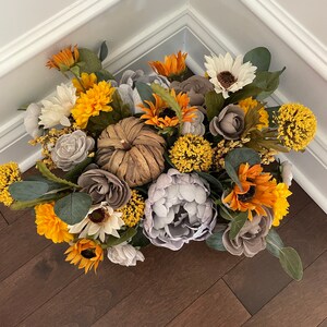 Peut inclure: Un arrangement floral sur le th&egrave;me de l'automne avec des tournesols, des pivoines grises et une petite citrouille rustique. L'arrangement est dans un r&eacute;cipient brun et est entour&eacute; de verdure.
