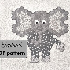 Peut inclure: Un bloc de courtepointe en forme d'éléphant en patchwork gris et blanc avec un motif de pois sur le corps et un motif de cœur sur les oreilles. Le bloc est composé de carrés de tissu cousus ensemble en forme hexagonale. Le texte "Elephant PDF pattern" est écrit en noir sur un fond gris.