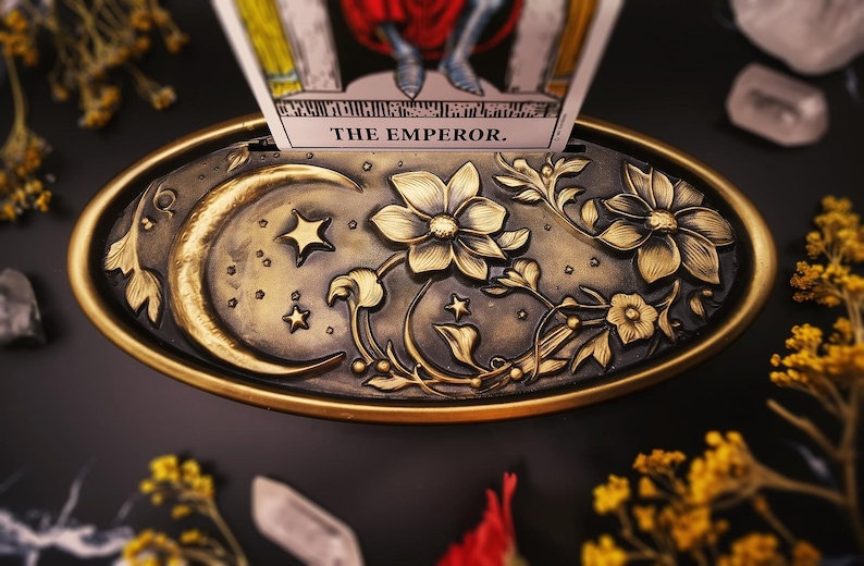 Op de afbeelding: Een gouden metalen dienblad met een sierlijk ontwerp met een halve maan, sterren en bloemmotieven. Het dienblad is ontworpen om een tarotkaart te houden, die zichtbaar is op de afbeelding en "THE EMPEROR." leest.