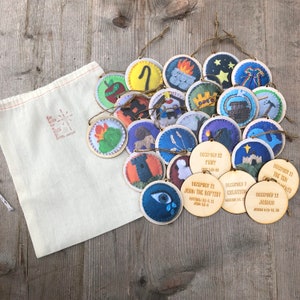 May include: A set of 24 wooden ornaments with felt appliques depicting scenes from the Bible. Each ornament has a different scene and scripture reference. The ornaments are packaged in a white drawstring bag.