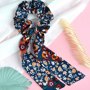 May include: A blue and orange floral patterned hair scrunchie with a matching tie. The scrunchie is made of soft fabric and has a gathered design.