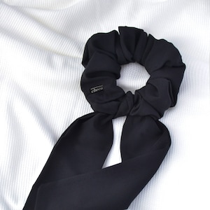May include: Black scrunchie with a long, black ribbon tail. The scrunchie has a small, black label with the word "cheeci" on it.