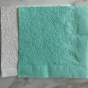 Puede incluir: Dos servilletas de papel con dise&ntilde;os de copos de nieve en relieve. Una servilleta es blanca y la otra de color verde azulado claro. La servilleta verde azulado tiene un borde texturizado. Adecuadas para eventos de invierno o festivos.