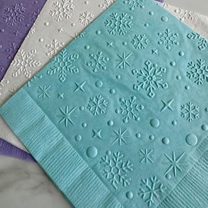 May include: Three decorative paper napkins in shades of purple, white, and blue. Each napkin features an embossed snowflake design with stars and circles. The napkins are ideal for winter-themed events or holiday gatherings.