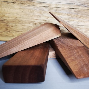 May include: Four wooden doorstops in various sizes and shapes. The doorstops are made of dark brown wood and have a smooth, polished finish.