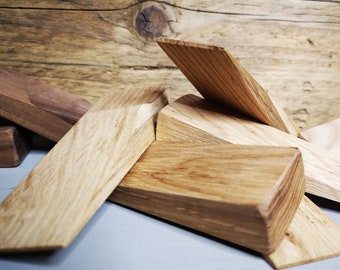 May include: A set of wooden wedges in various sizes and shapes, made of light brown wood with a natural grain pattern. The wedges are arranged on a gray surface.