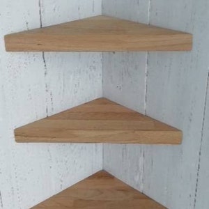 May include: Three wooden corner shelves in a triangular shape. The shelves are made of light brown wood and are mounted on a white wall.