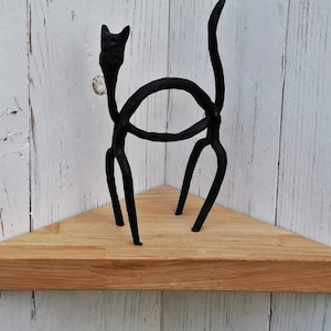 May include: A triangular wooden shelf with a black metal cat sculpture on top. The shelf is made of natural wood and has a light brown color.