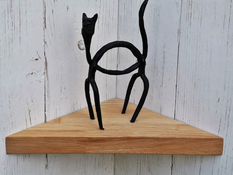 May include: A triangular wooden shelf with a black metal cat sculpture on top. The shelf is made of natural wood and has a light brown color.