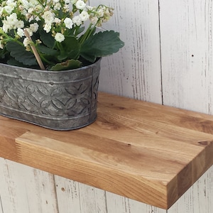 May include: A natural wood shelf with a rustic finish. A metal planter with white flowers sits on the shelf.