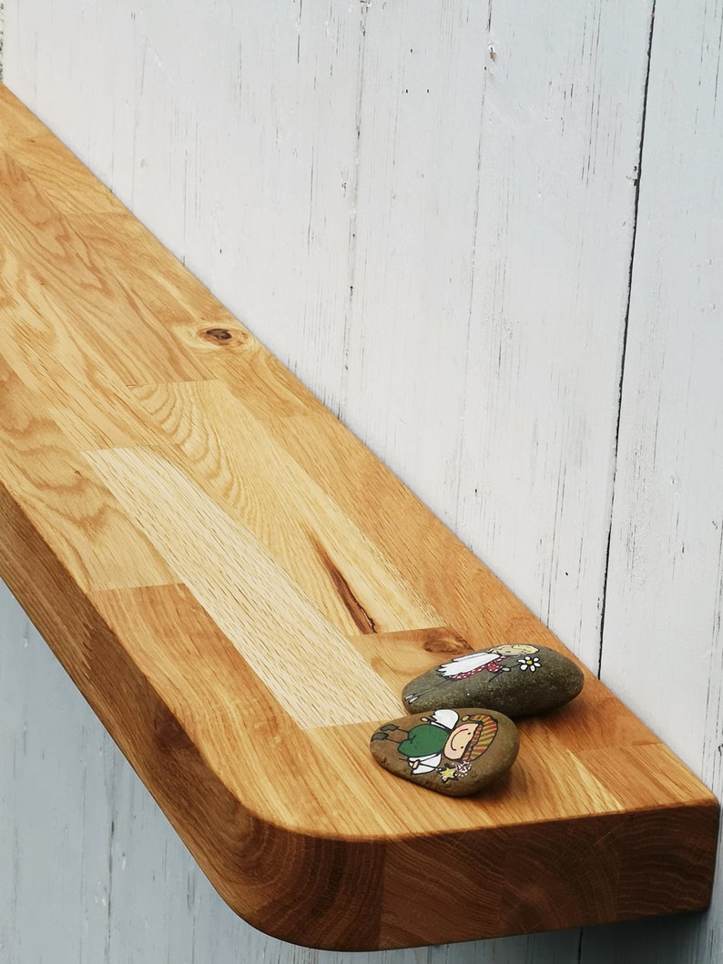 Pu&ograve; includere: Un ripiano in legno curvo con finitura in legno naturale. Due pietre dipinte con disegni fantasiosi sono posizionate sullo scaffale.