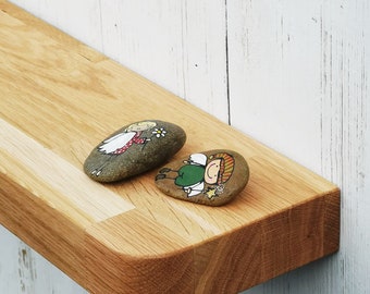Könnte beinhalten: Ein Holzregal mit abgerundeten Kanten ist an einer weißen Wand montiert. Zwei bemalte Steine, einer mit einem Mädchen und der andere mit einem Jungen, liegen auf dem Regal.