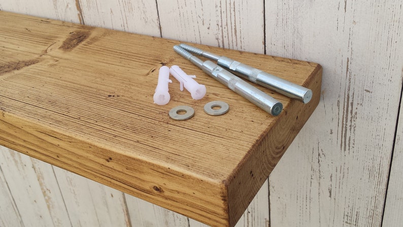May include: A rustic wooden shelf with a natural finish. The shelf is made of reclaimed wood and has a distressed look. It comes with two metal brackets and four plastic anchors for mounting.