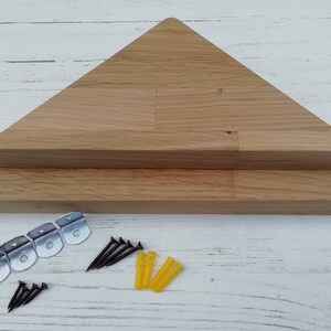 May include: Two wooden triangular shelves with rounded edges, made of light brown wood. The shelves are stacked on top of each other. The shelves are accompanied by mounting hardware, including screws, anchors, and metal brackets.