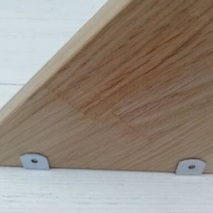 May include: Close-up of a wooden triangle shelf with two metal brackets attached to the bottom.