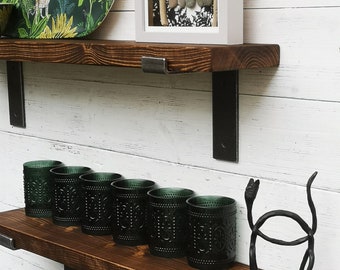 May include: Two wooden shelves with black metal brackets. The top shelf has a green and yellow tray with a jungle print and a framed picture with the text "dream big" and a family of five made of stones. The bottom shelf has six green glass candle holders and a black metal sculpture of a cat.