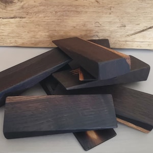 May include: A set of six black wooden wedges, likely used as furniture risers or shims. The wedges are made of dark wood with a natural grain pattern.
