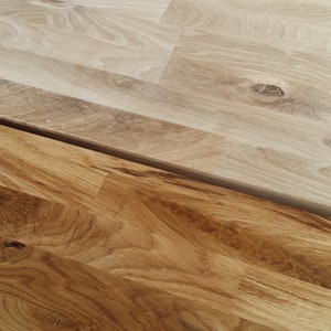 May include: Two pieces of wood flooring, one stained a darker brown and the other left in its natural light wood color. The wood grain is visible in both pieces.