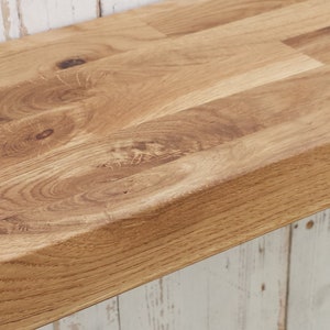 May include: A close-up of a light brown wooden shelf with a natural wood grain finish. The shelf is made of multiple pieces of wood that are joined together with a tongue and groove joint.