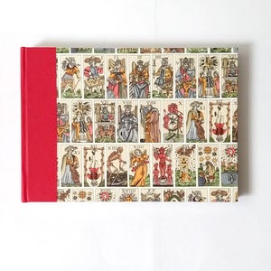 Puede incluir: Una taza de cerámica blanca con asa negra y el texto "But First, Coffee" en negrita negra. La taza se encuentra sobre un fondo borroso, sugiriendo un ambiente acogedor.