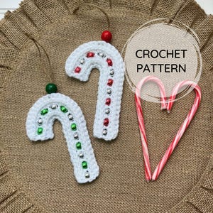 May include: Two white crochet candy cane ornaments with red and silver bead accents and a green bead at the top. The text "CROCHET PATTERN" is in a circle. Two candy canes form a heart.