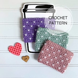 Könnte beinhalten: Drei gehäkelte Kaffeetassen-Cozies in Lila, Grün und Rosa mit weißen Herzen. Die Cozies sind übereinander gestapelt und der Text "CROCHET PATTERN" ist im Hintergrund sichtbar.