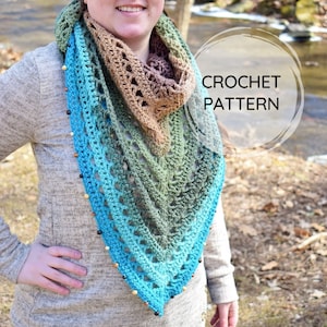 May include: A crochet shawl with a gradient of brown, green, and blue colors. The shawl has a delicate lace pattern and is adorned with wooden beads along the edges. The text "CROCHET PATTERN" is written in a circle on the image.