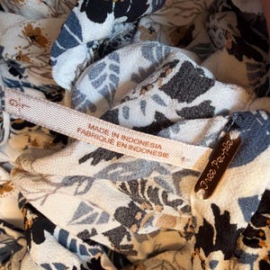 Puede incluir: Primer plano de una tela estampada con flores con una etiqueta que dice "Made in Indonesia Fabriqu&eacute; en Indonesie". La tela tiene una mezcla de dise&ntilde;os florales blancos, negros, azules y beige. Tambi&eacute;n es visible una peque&ntilde;a etiqueta marr&oacute;n con "Free People".