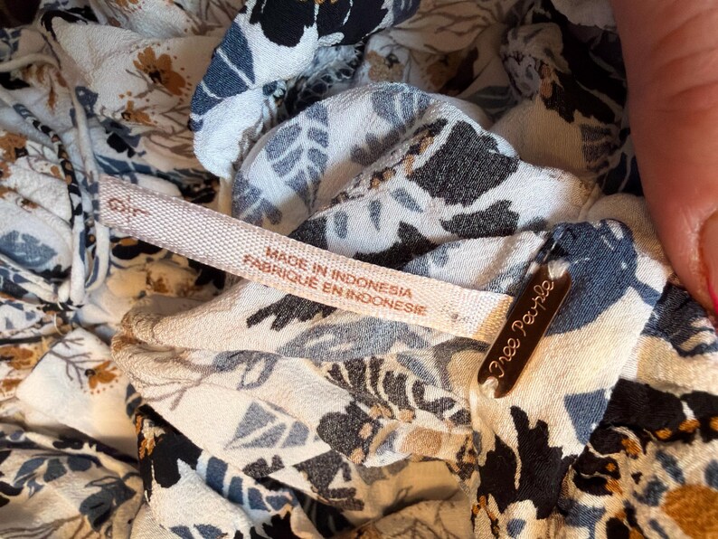 Puede incluir: Primer plano de una tela estampada con flores con una etiqueta que dice "Made in Indonesia Fabriqu&eacute; en Indonesie". La tela tiene una mezcla de dise&ntilde;os florales blancos, negros, azules y beige. Tambi&eacute;n es visible una peque&ntilde;a etiqueta marr&oacute;n con "Free People".
