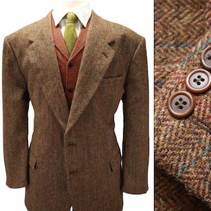 May include: A brown herringbone tweed blazer featuring a two-button front closure, notched lapels, and side pockets. The blazer is layered over a rust-colored vest and a white collared shirt with a green tie. The sleeve cuff displays three brown buttons.